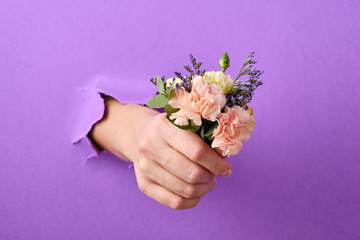 Hand with flowers is thrust through a hole in the paper background