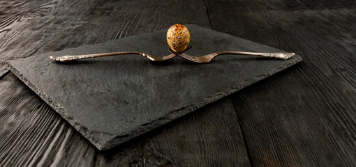 Quail egg on two old crossed forks on a kitchen cutting board.