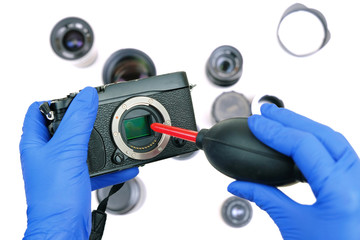hands cleaning digital mirrorless camera sensor from dust with air blower