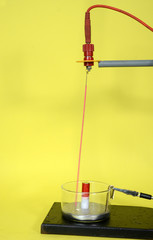 Closeup on Faraday motor demonstration arrangement with mercury pool and a light red conducter that moves in circles around a magnet when a current flows.