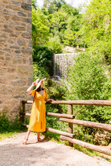 young stunning woman in yellow sundress with big hat outdoors at sunny day waterfall on background