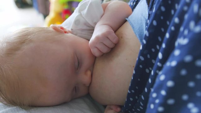 Close up of blue eyed new born baby breastfeeding and grabbing the breast to release more milk