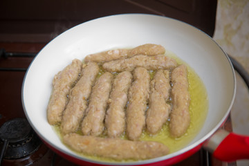 The long cutlet is fried in a red pan. She cooks the cutlet in a white pan.