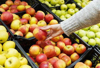 Closeup image of a woman selecting apples from the food counter at the supermarket.