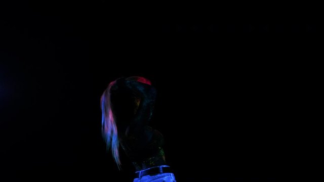 Girl Colored by Fluorescent powder. Unreal, Stylish Vivid Make-Up or Body Art, Glowing in Ultraviolet Lamp. Flexy Female Dancing and Throws Up her Purple Hair. Reaching Arms, Blue Eyes in Lenses.