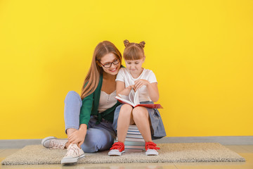 Cute little girl and her mother reading books near color wall