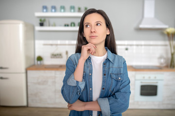 Fototapeta premium Thoughtful young woman standing in her kitchen