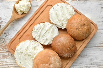 Fresh buns with tasty cream cheese on white wooden background