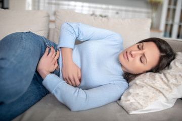 Obraz na płótnie Canvas Woman lying on a sofa and having a stomach ache