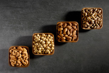 Hazelnuts, almonds, pistachios and cashews in the wooden bowls on the gray stone texture with copy space