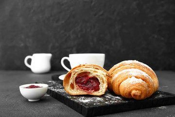 Board with tasty sweet croissants and jam on dark background