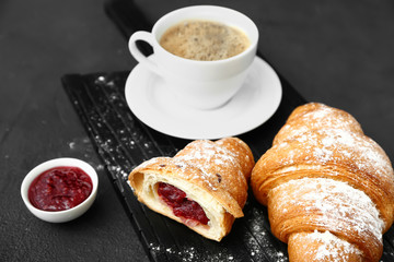 Board with tasty sweet croissants, coffee and jam on dark background