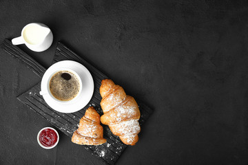 Board with tasty sweet croissants, coffee and jam on dark background