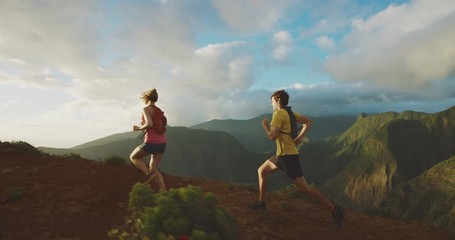 Young athletic man and woman running together outdoors on a mountain top at sunset, two friends exploring the mountains together, weekend summer adventures