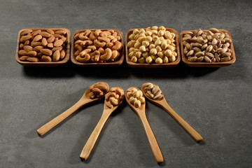 Bowls of nuts and the nuts in the wooden spoons on stone texture, still life