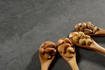 Hazelnuts, almonds, pistachios and cashews in the wooden spoons on stone texture
