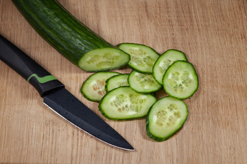 Fresh green cucumber is cut into mugs and lies on the kitchen board next to a ceramic knife. The element of the vegetarian menu.