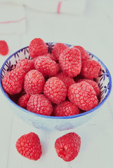 Fresh raspberries in a blue bowl on a white background.