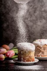 Sugar powder pouring on glazed easter cake on dark rustic background