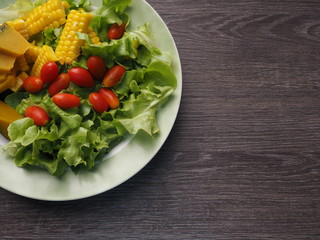Top view green red and yellow colored vegetable salad in dish on wooden table. Free copy space for text on right hand.
