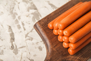Boiled sausages on a concrete background close-up. Raw sausages from the store on a wooden board and copy space.