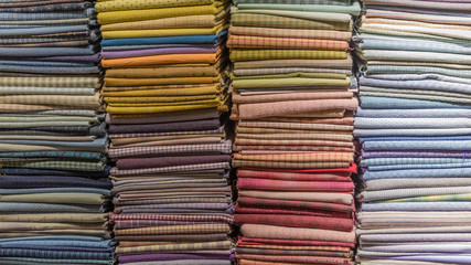 Fabric scarves and shawls of different colors, textures and patterns are stacked in vertical stacks. Background image.