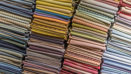 Fabric scarves and shawls of different colors, textures and patterns are stacked in vertical stacks. Background image.