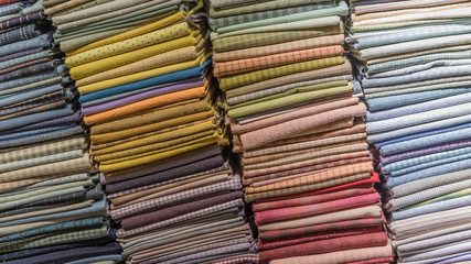 Fabric scarves and shawls of different colors, textures and patterns are stacked in vertical stacks. Background image.