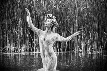 Fototapeta na wymiar Romantic woman in flower hoop at hair, lace transparent dress in lake 