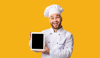 Happy Chef Showing Digital Tablet Screen On Yellow Studio Background
