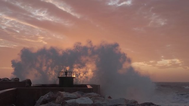 Schizzi e spruzzi del mare che si infrangono sul faro del porto al tramonto. Super slow motion.