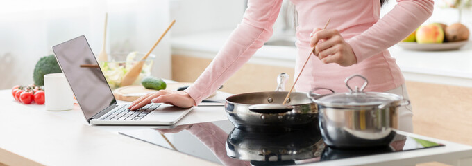 Woman cooking lunch according to recipe on laptop