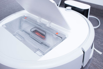 white robot vacuum cleaner is charging on the charger on laminate floor cleaning dust in living room interior. Smart electronic housekeeping technology.