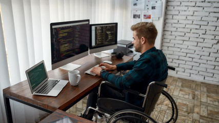 Professional programmer. Side view of young concentrated web developer in a wheelchair writing...