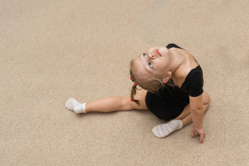 3 years old girl in a black gymnastics leotard beautifully arched on a light carpet in the gym
