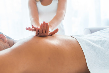 Portrait Of Man Receiving Massage Treatment From Female Hand. Close-up of masseur's hands and a client's back. Man getting relaxing massage in spa. Man receiving back massage from masseur
