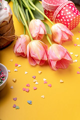 Easter cake with tulips and baking items on yellow background with copy space
