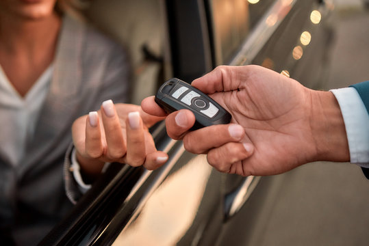 Good choice. Cropped photo of male hand giving the car key to woman sitting in the car