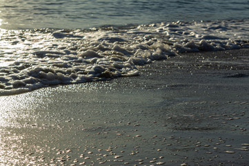 View of foamed waves against sunlight at sunset near shore. Selective focus. Close-up. Nature concept for design.