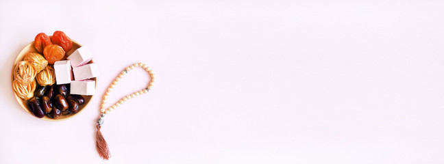 Sweets, dates, dried apricots on a plate on a pink background. © Guzel