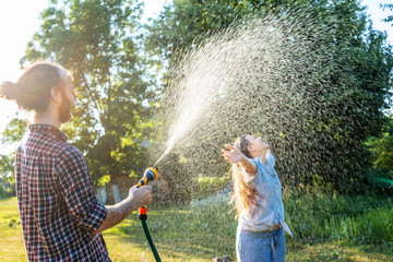 young happy beautiful couple hosing in the garden, summer happiness and love concept, poured water...