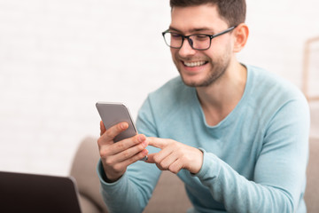 Obraz na płótnie Canvas Joyful Guy Using Smartphone Texting Sitting On Couch At Home