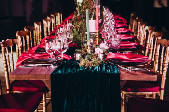 in the dark hall there are festive tables and chairs, tables decorated with compositions of flowers, greenery and candles. On the tables are glasses, plates and cutlery