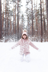 Fototapeta na wymiar A beautiful pretty young girl with curly hair and a snow-white smile in a pink fur coat is walking and fooling around in the winter forest against the background of snow and trees, enjoy