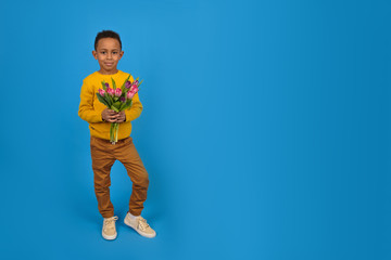 Fototapeta na wymiar Portrait of a smiling African American boy with a bouquet of tulips for mom spring flowers on a blue background. Concept of greeting mother's Day, father's day, Valentine's day gift for a woman.