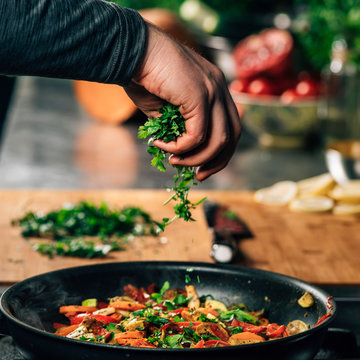 Hand Adding Parsley into Frying Pan with Vegetables