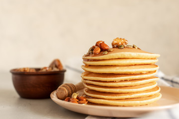 Stack of delicious pancakes with chocolate, honey, nuts and slices of banana on plate and napkin on wooden background