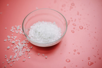 sea salt in a glass bowl on a pink pastel background next to sea water