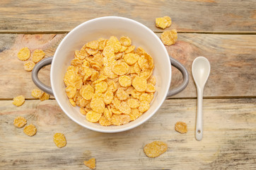 Bowl of cornflakes with a white spoon on a wooden background