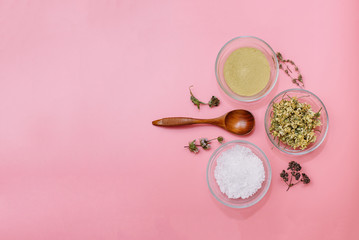 Obraz na płótnie Canvas Close up of Ingredients of ayurvedic treatment or face pack. Yellow clay, turmeric powder and dried chamomile, sea coarse salt in glass cups on a pink pastel colour background. Flat lay with copyspace